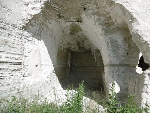 Cave house carved into white limestone in Benamaurel, Granada, with natural rock formations and gree.