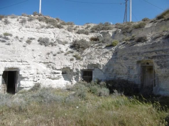 Cave house with barred windows in Benamaurel, Granada, set in a rocky landscape.