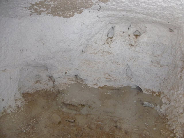 Interior view of a cave house in Benamaurel, Granada, showing rough stone walls and earthy floor.