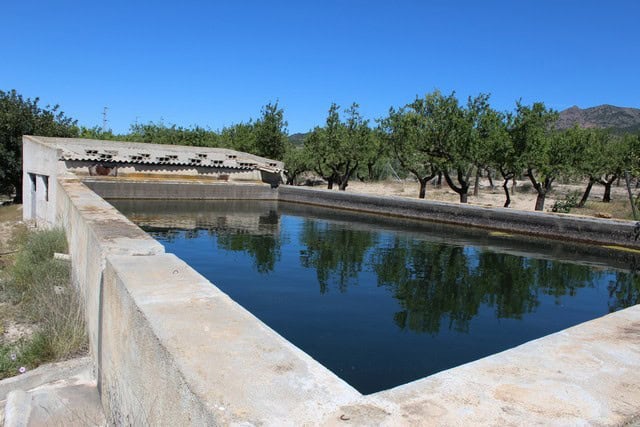 Traditional water reservoir in Lucar, Almeria, surrounded by lush trees and scenic mountain views.