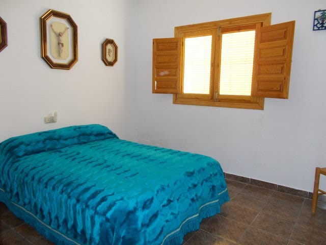 Interior view of a bedroom in a rural property in Caniles, Granada, with a blue bed and wooden windo.