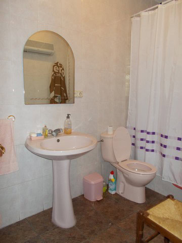 Bathroom with sink, mirror, toilet, and shower curtain in rural Caniles property.
