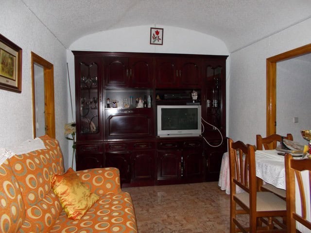 Charming cave house living room with traditional decor in Bacor, Granada, featuring wooden furniture.