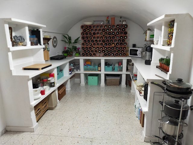 Cave house kitchen with white shelves, colorful decor, and storage in Benamaurel, Granada.