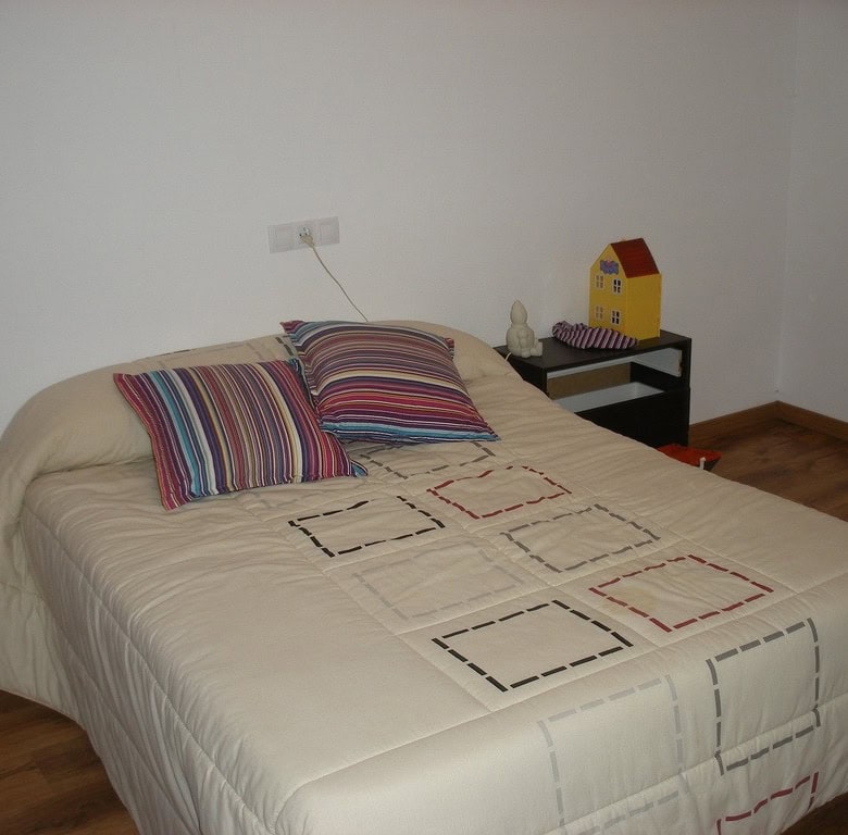 Cave house bedroom with simple decor and colorful pillows, located in Benamaurel, Granada.