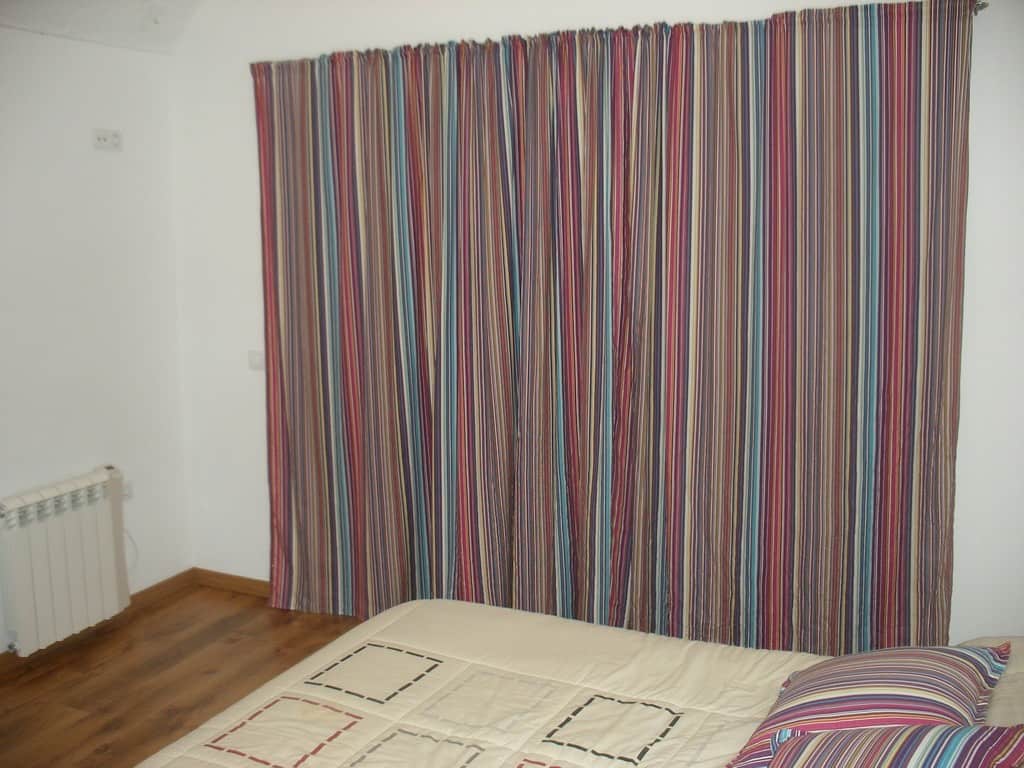 Interior view of a bedroom with striped curtains and a simple bed setup.