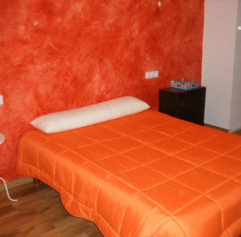 Beautiful bedroom in a cave house with orange walls and modern furnishings in Benamaurel, Granada.