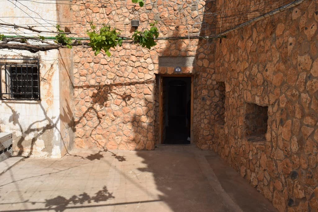 Cave house entrance in Baza, Granada with rustic stone walls and shaded courtyard.