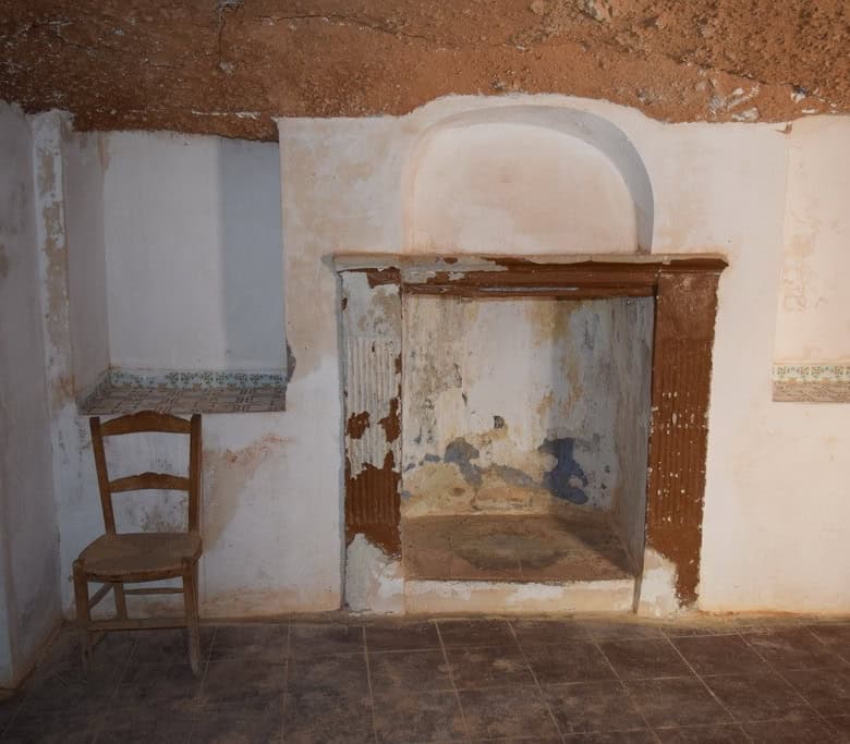 Traditional cave house interior in Baza, Granada, showcasing rustic walls and a simple fireplace.