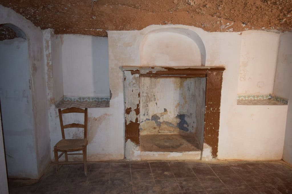 Traditional cave house interior in Baza, Granada, showcasing rustic walls and a simple fireplace.