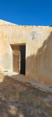 Rural property entrance with rustic wooden door in Benamaurel, Granada, under a clear blue sky.