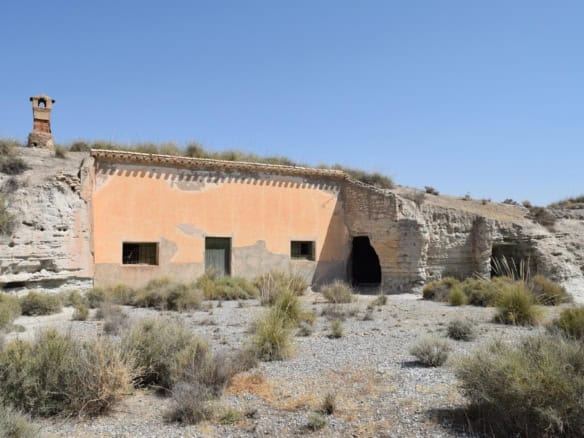 Cave house in Baza, Granada, built into the hillside with a chimney and small windows, surrounded by.