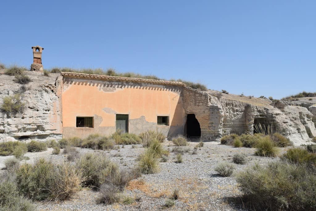 Cave house in Baza, Granada, built into the hillside with a chimney and small windows, surrounded by.