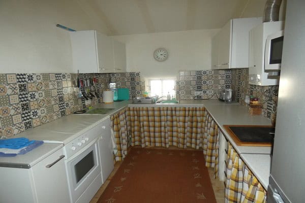Charming kitchen in Gor village, Granada with white cabinets, patterned tiles, and cozy checkered cu.
