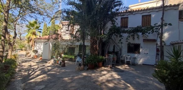 Cave house in Caniles, Granada, with outdoor seating and lush greenery.