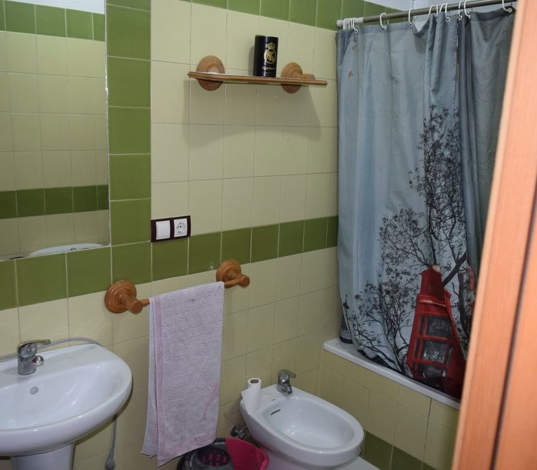 Cozy bathroom inside a cave house with green tiled walls, sink, bidet, and shower curtain in Cuevas.