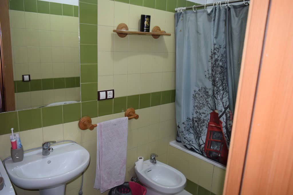 Cozy bathroom inside a cave house with green tiled walls, sink, bidet, and shower curtain in Cuevas.