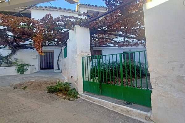 Rural property in Don Pedro, Jaen, featuring a white house with a green gate and lush grapevines ove.