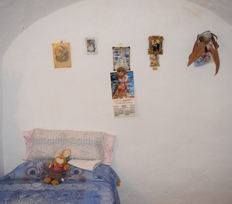 Cave house interior with decorated white walls and cozy bed with plush toys.
