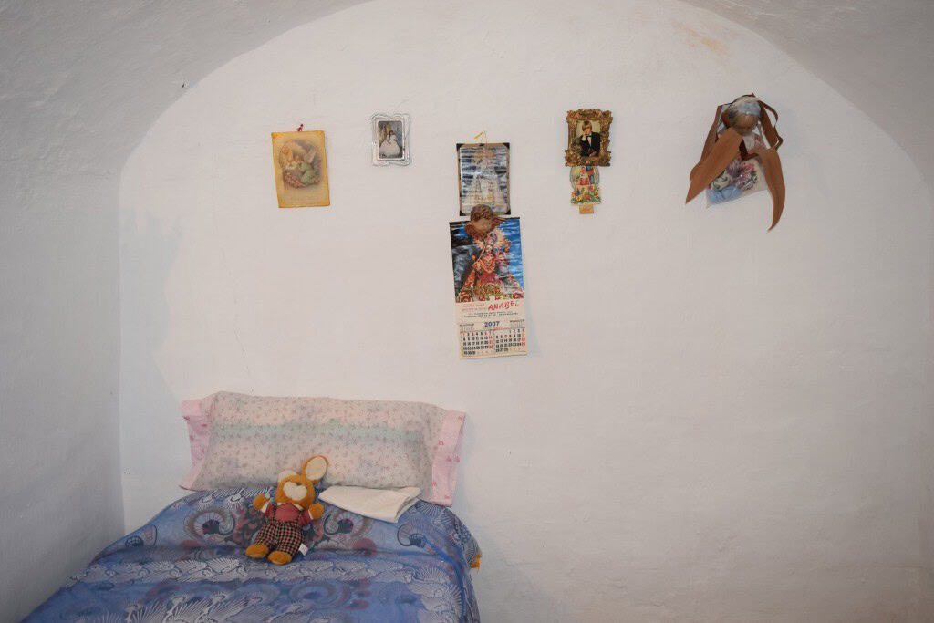 Cave house interior with decorated white walls and cozy bed with plush toys.