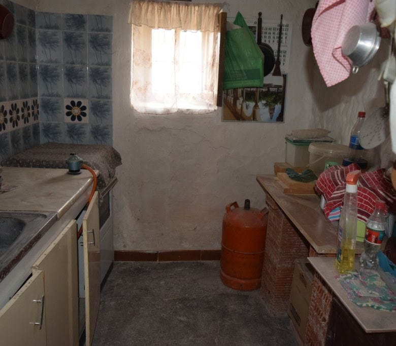 Charming cave house interior in Benamaurel, Granada, showcasing rustic kitchen with simple furnishin.