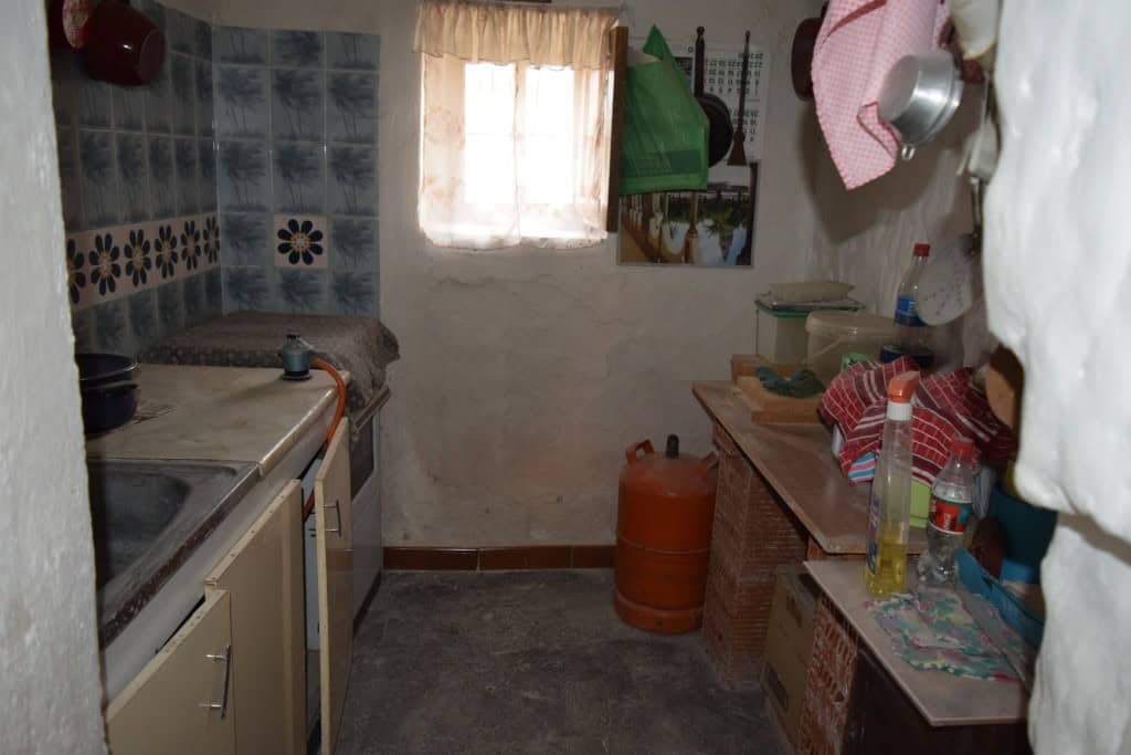 Charming cave house interior in Benamaurel, Granada, showcasing rustic kitchen with simple furnishin.