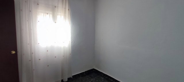 Interior view of a simple, bright room with white walls and a window with sheer curtains in Tijola,.