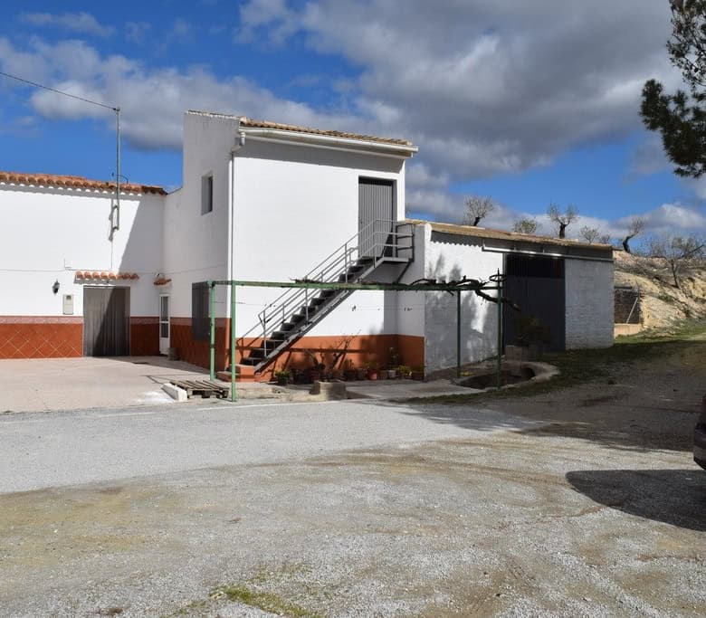 Cave house with white exterior walls and outdoor staircase in Cuevas del Campo, Granada. Scenic rura.
