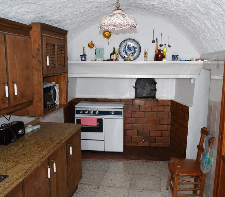 Cozy cave house kitchen with rustic wooden cabinets and vintage decor in Cuevas del Campo, Granada.