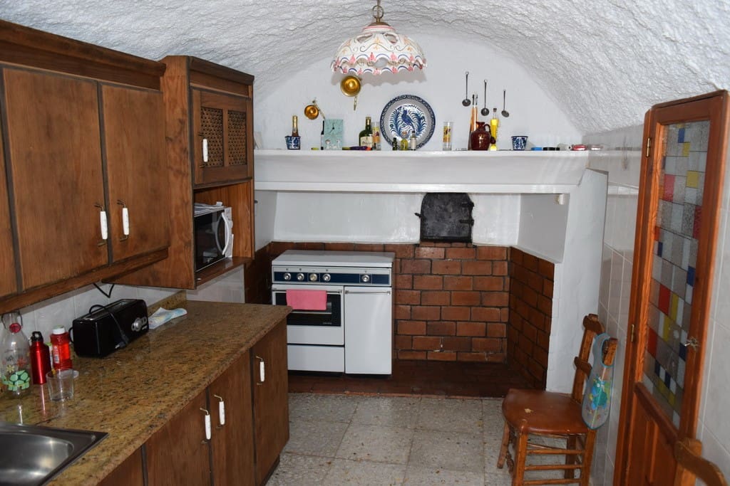 Cozy cave house kitchen with rustic wooden cabinets and vintage decor in Cuevas del Campo, Granada.