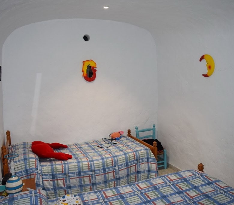 Cozy cave house bedroom with whitewashed walls and colorful decor in Cuevas del Campo, Granada.