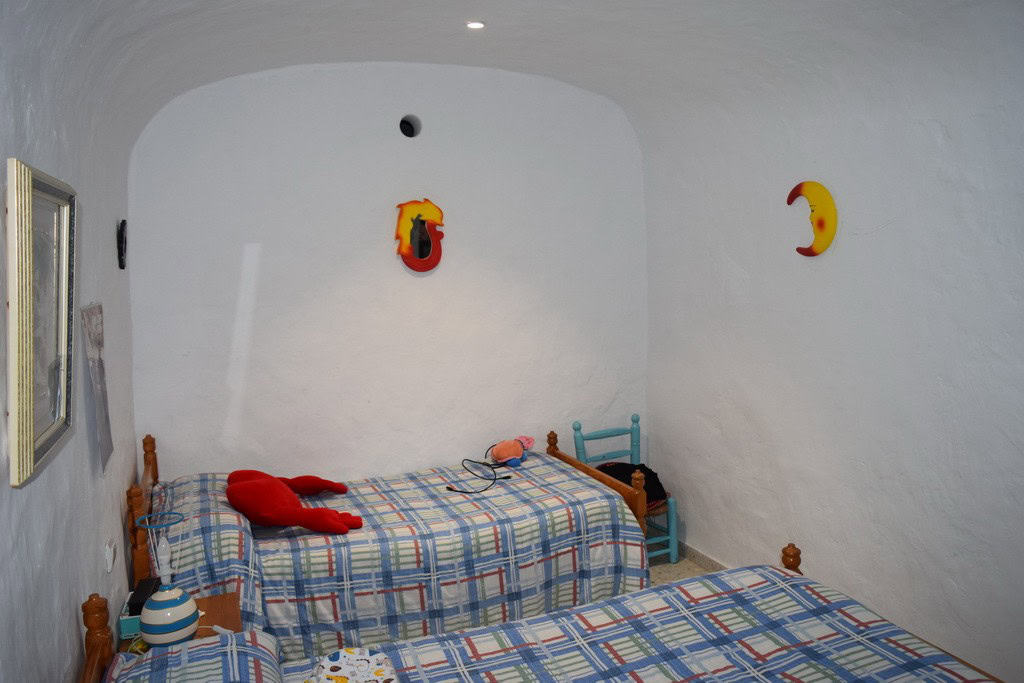 Cozy cave house bedroom with whitewashed walls and colorful decor in Cuevas del Campo, Granada.