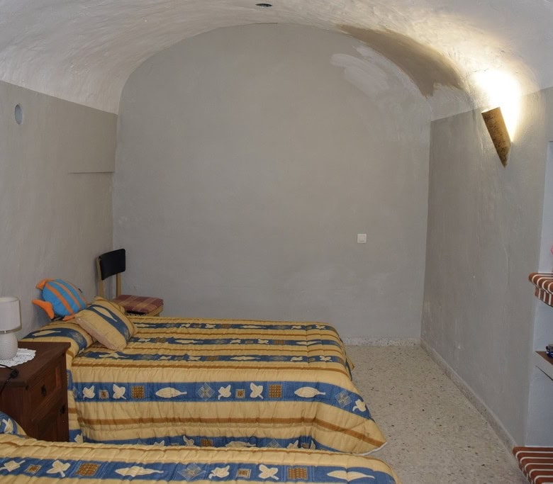 Cave house interior with two beds, rustic decor, and arched ceiling in Cuevas del Campo, Granada.