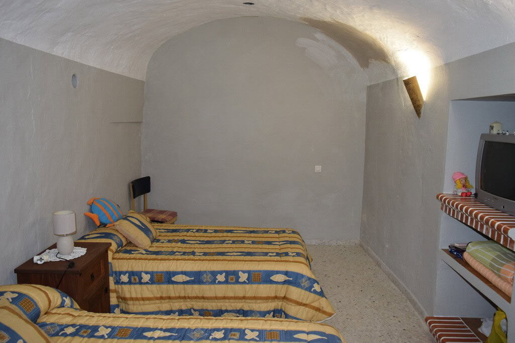 Cave house interior with two beds, rustic decor, and arched ceiling in Cuevas del Campo, Granada.