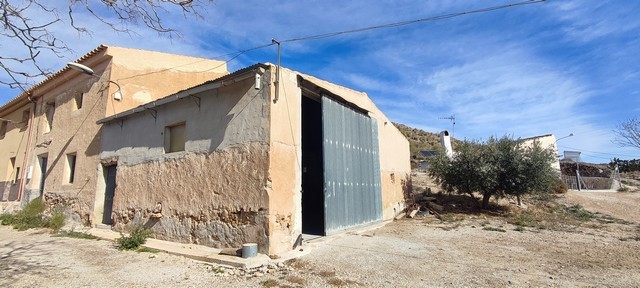 Traditional rural house in Jamula, Granada, with rustic walls and a metal barn door.