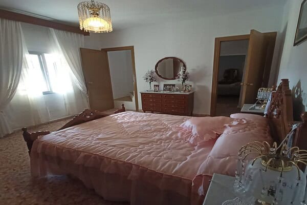 A charming bedroom featuring a large bed with pink bedding, vintage furniture, and natural light fro.