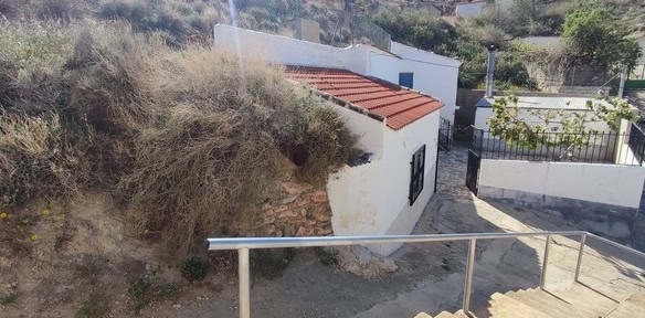 Cave house in Caniles, Granada with white walls and red-tiled roof, set on a hillside.