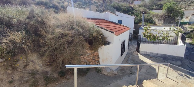 Cave house in Caniles, Granada with white walls and red-tiled roof, set on a hillside.