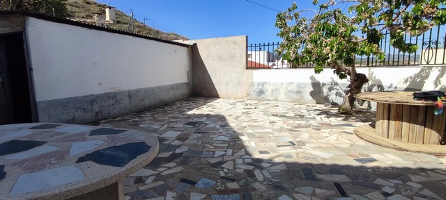 Cave house outdoor patio in Caniles, Granada with stone flooring and a small tree.