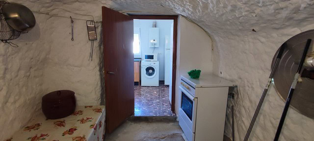 Unique cave house interior in Caniles, Granada, with basic kitchen and cozy sleeping area.