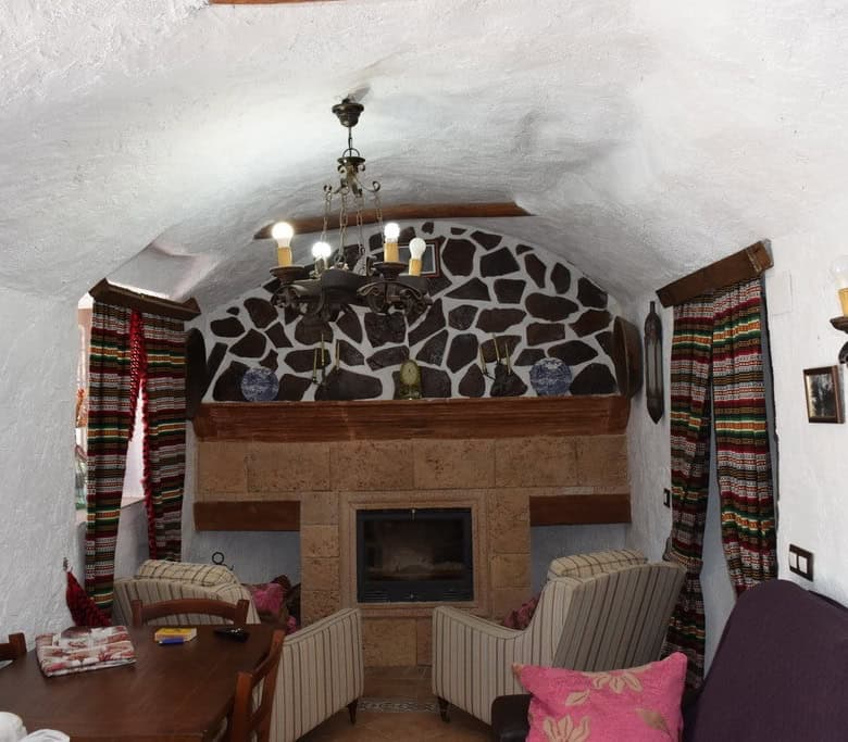 Charming cave house living room with stone fireplace and rustic decor in Granada, Spain.