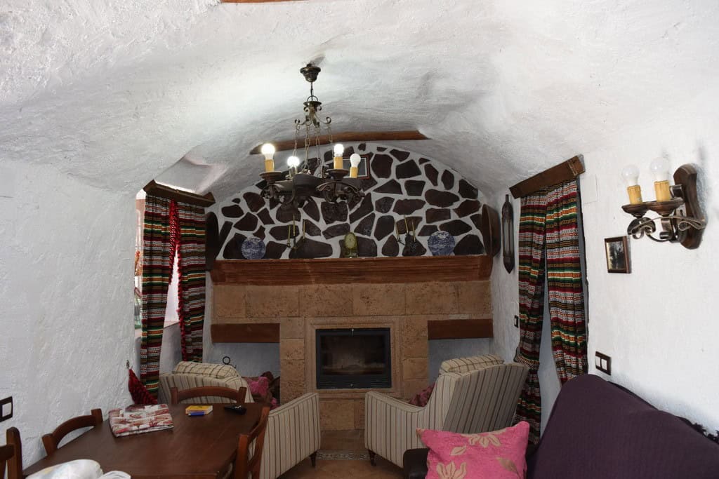 Charming cave house living room with stone fireplace and rustic decor in Granada, Spain.