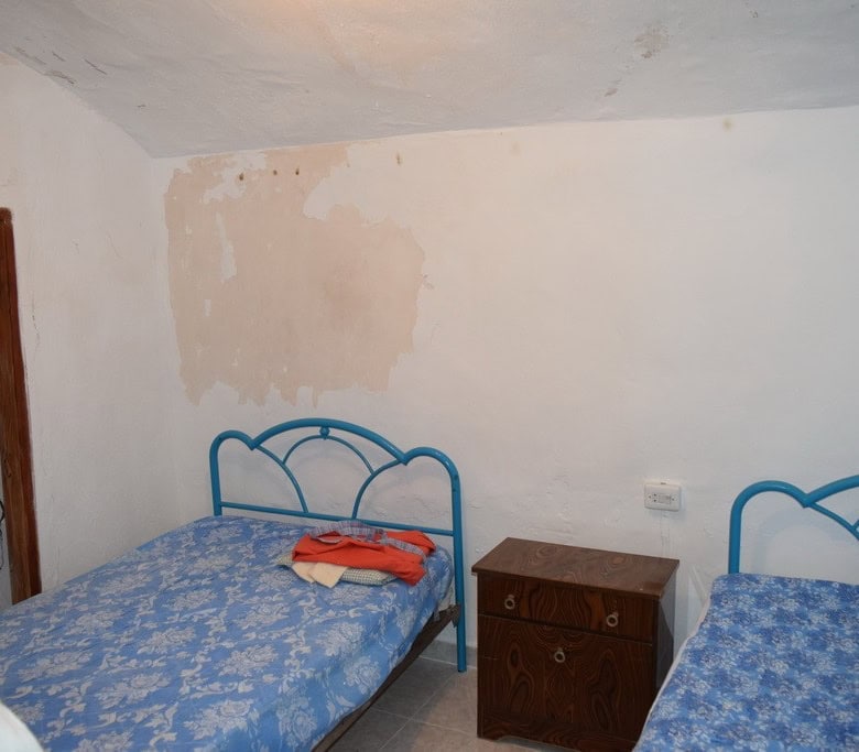 Cave house interior with two beds and a small wooden nightstand in Bacor, Granada.