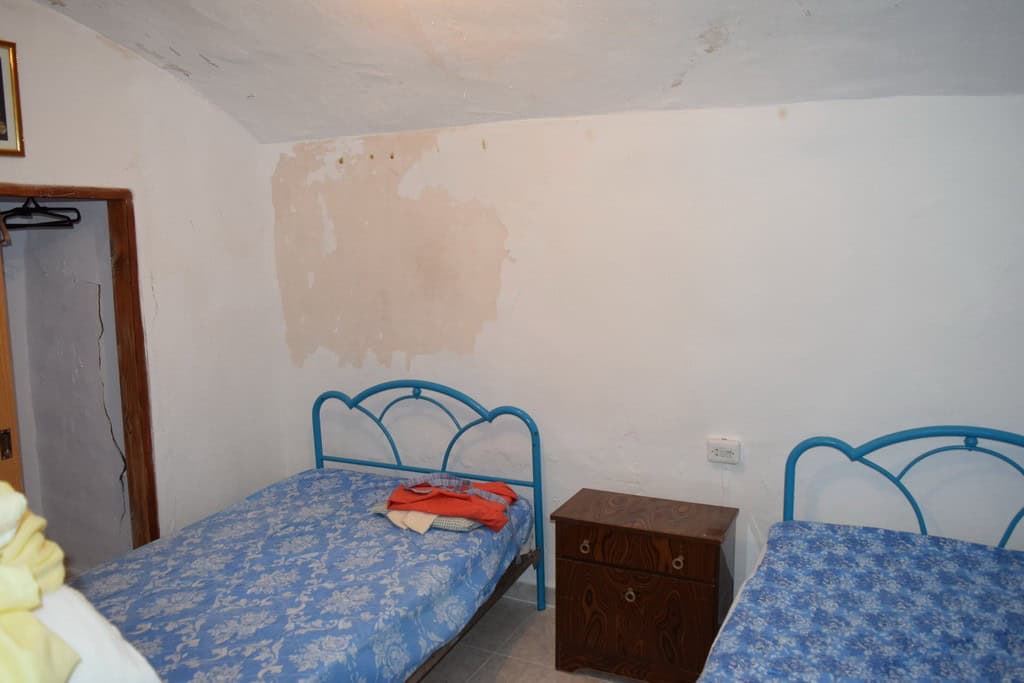 Cave house interior with two beds and a small wooden nightstand in Bacor, Granada.