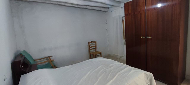 Interior view of a simple bedroom in a village property in Bayarque, Almeria, featuring a bed, chair.