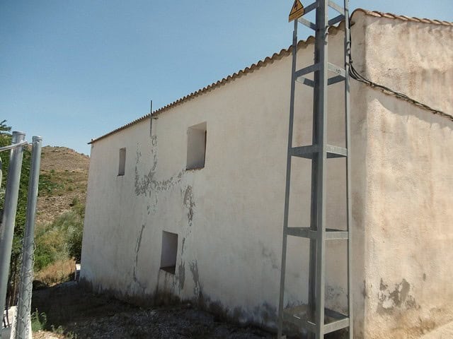 Traditional whitewashed rural house in Hijate, Almeria, with a simple exterior and scenic hillside b.