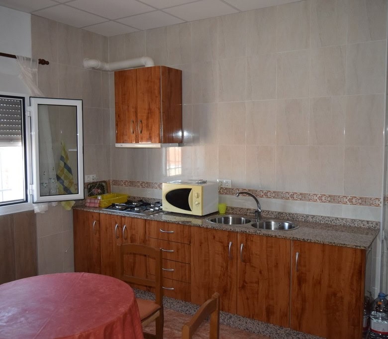 Cave house kitchen with wooden cabinets, microwave, and refrigerator in Castillejar, Granada.