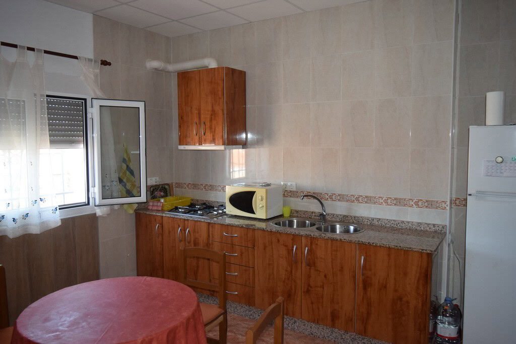 Cave house kitchen with wooden cabinets, microwave, and refrigerator in Castillejar, Granada.