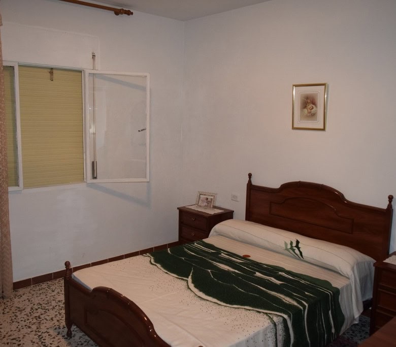Interior view of a cozy cave house bedroom in Castillejar, Granada, featuring a wooden bed and simpl.