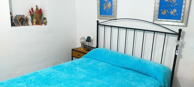 Cozy bedroom in a cave house located in Benamaurel, Granada, with a black metal bed and vibrant blue.